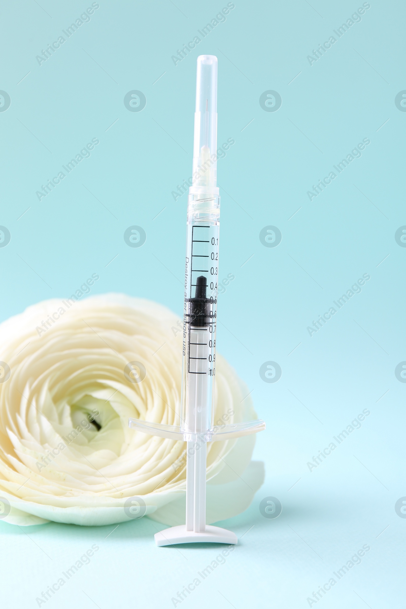 Photo of Cosmetology. Medical syringe and ranunculus flower on light blue background