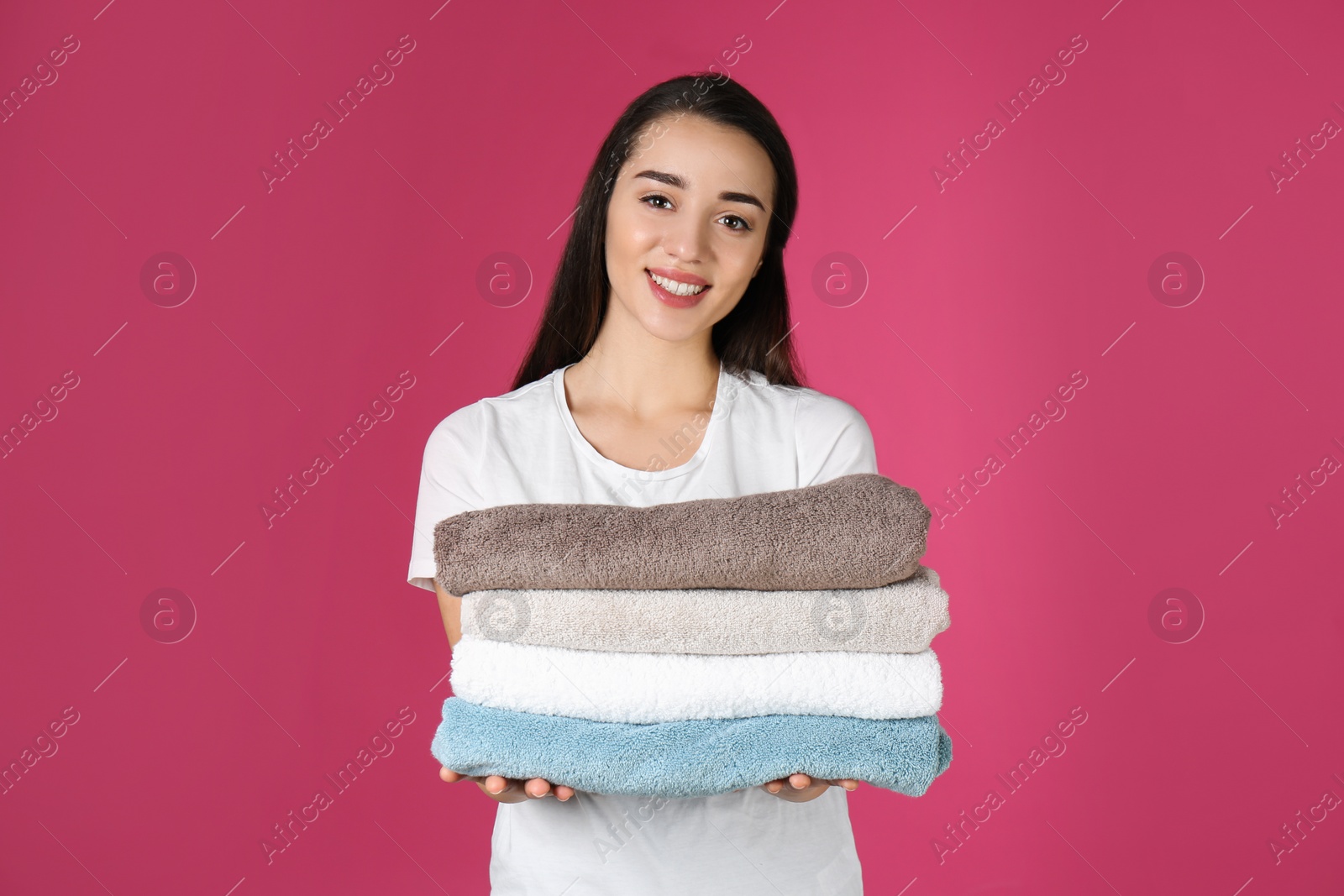 Photo of Happy young woman holding clean towels on color background. Laundry day