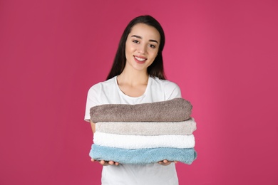 Photo of Happy young woman holding clean towels on color background. Laundry day