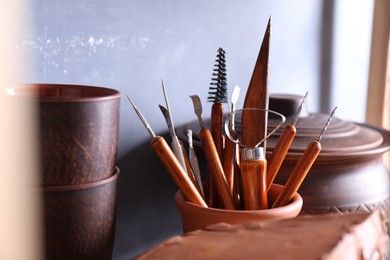 Photo of Set of different crafting tools and clay dishes on wooden rack in workshop, closeup