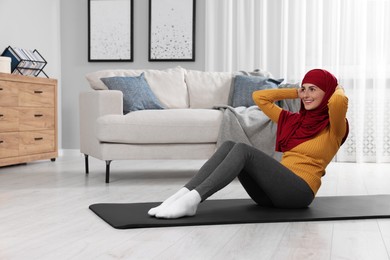 Photo of Muslim woman in hijab doing abs exercise on fitness mat at home. Space for text