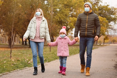 Family in medical masks walking outdoors on autumn day. Protective measures during coronavirus quarantine