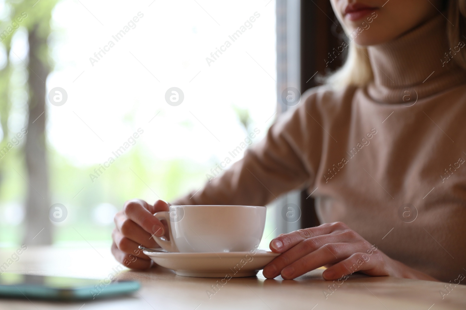 Photo of Young woman with cup of coffee at table in morning, closeup