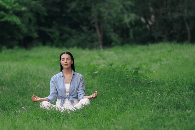 Photo of Young woman meditating on green grass. Space for text