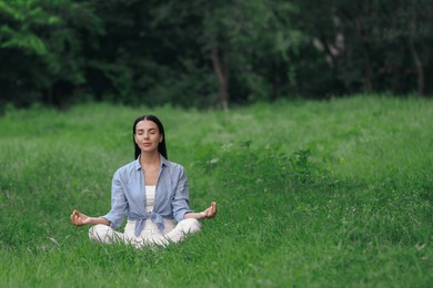 Young woman meditating on green grass. Space for text