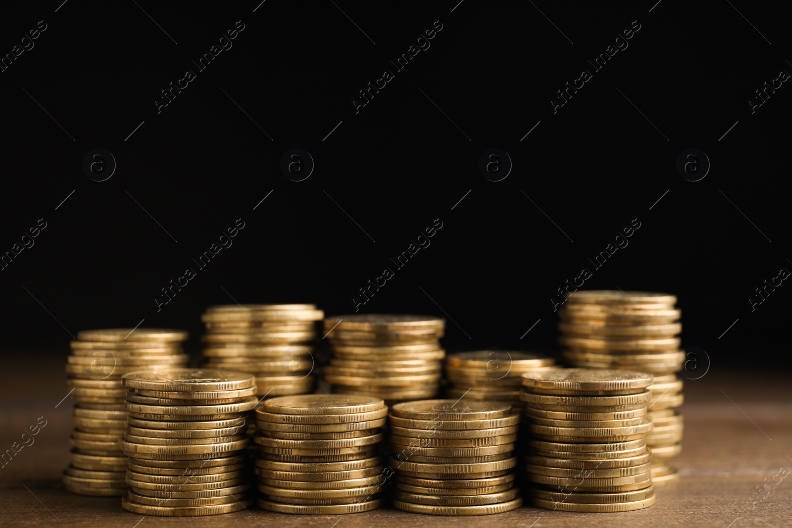 Photo of Many coins stacked on wooden table against black background, space for text