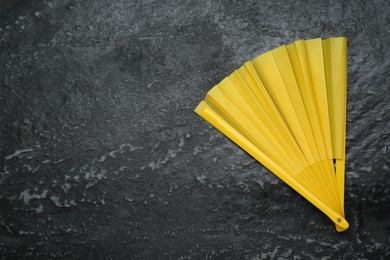 Photo of Bright yellow hand fan on grey textured background, top view. Space for text