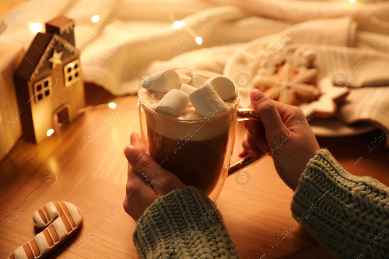 Photo of Woman holding cup of hot drink with marshmallows at wooden table, closeup. Magic Christmas atmosphere