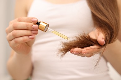 Photo of Woman applying oil hair mask indoors, closeup