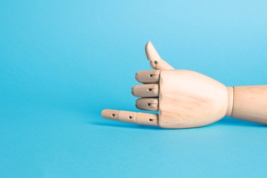 Photo of Wooden mannequin hand on light blue background. Space for text