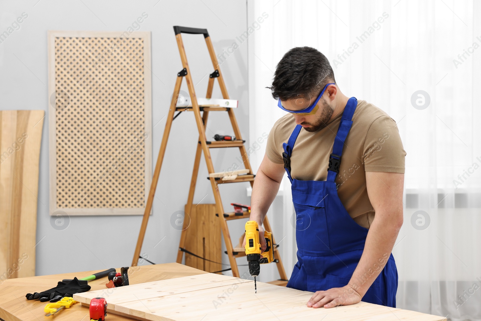 Photo of Young worker using electric drill at table in workshop