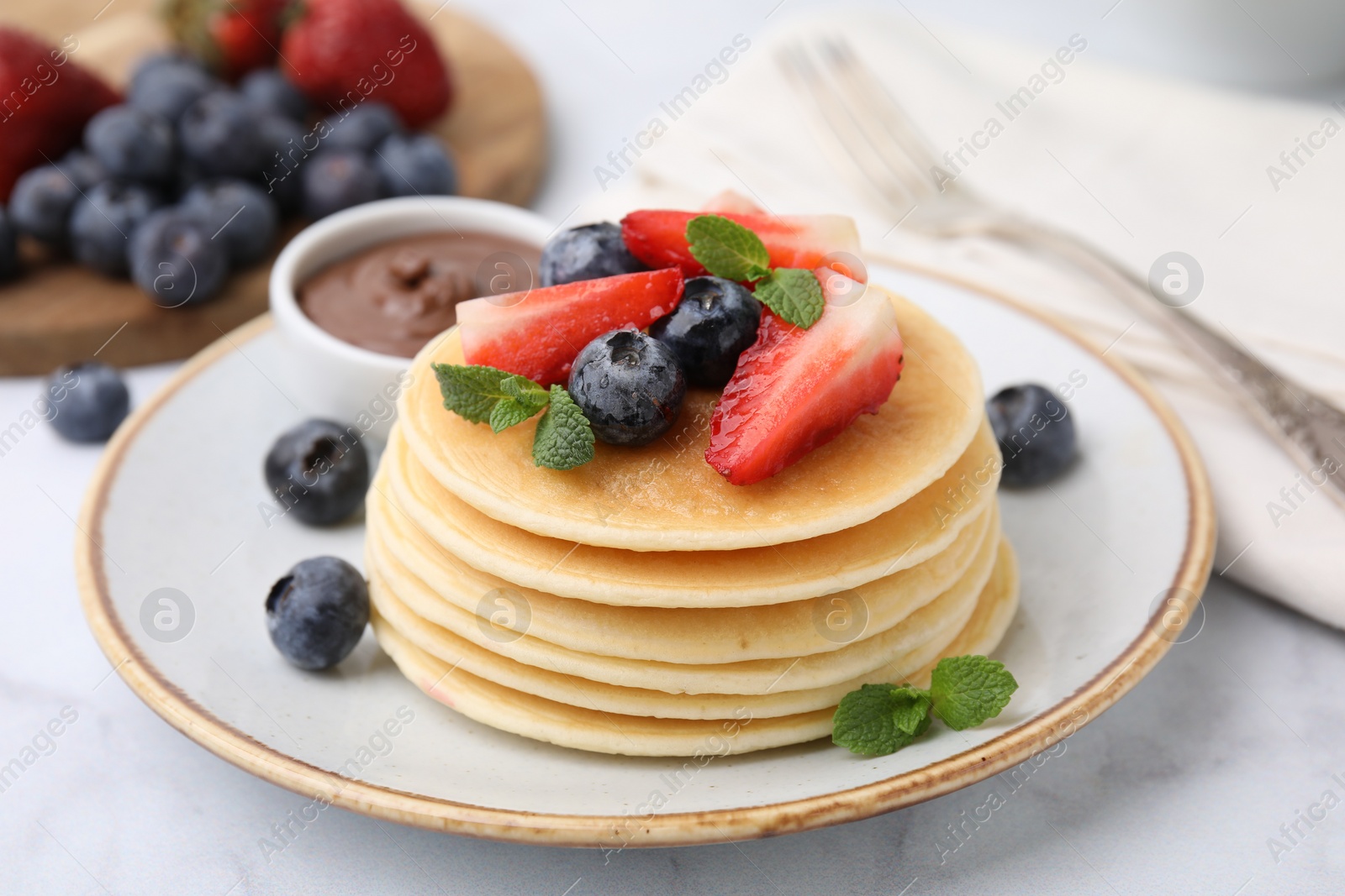 Photo of Delicious pancakes with strawberries, blueberries and chocolate sauce on light table, closeup