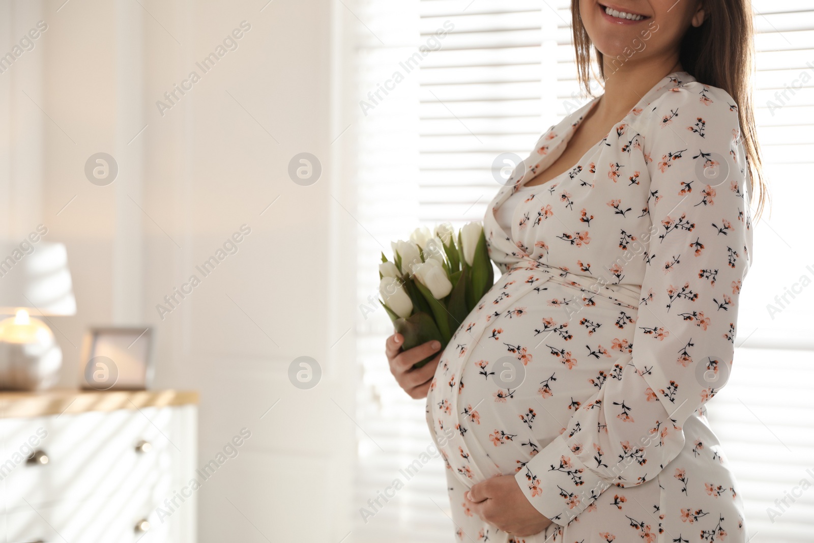 Photo of Young pregnant woman with flowers at home, closeup. Space for text