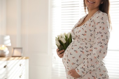 Young pregnant woman with flowers at home, closeup. Space for text