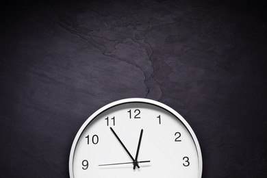 Photo of Stylish round clock on black table, top view with space for text. Interior element