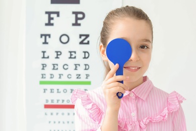 Photo of Cute little girl near eye chart in ophthalmologist office