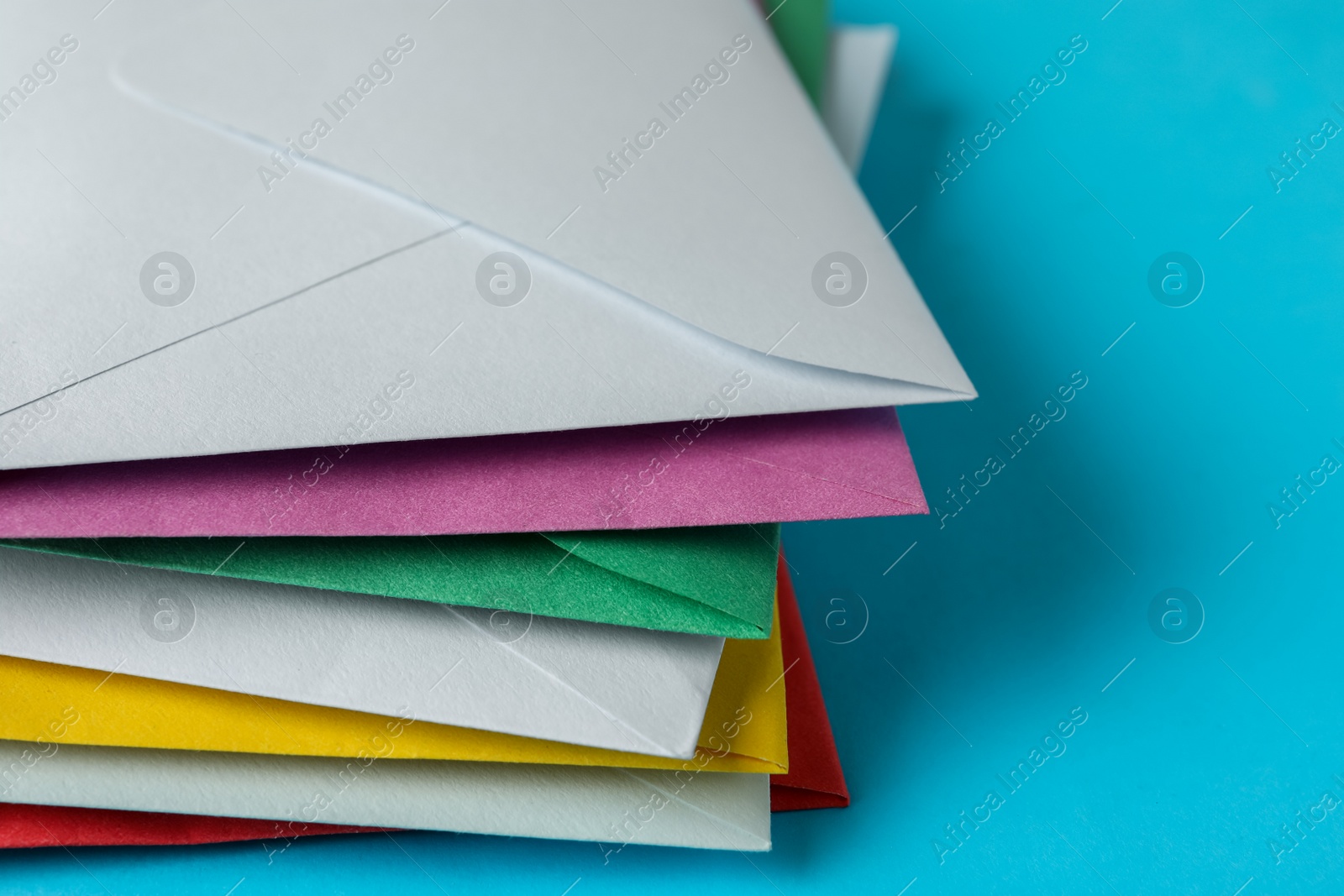 Photo of Stack of colorful paper envelopes on light blue background, closeup