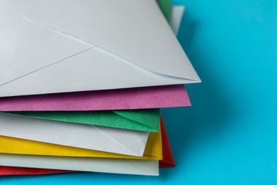 Stack of colorful paper envelopes on light blue background, closeup