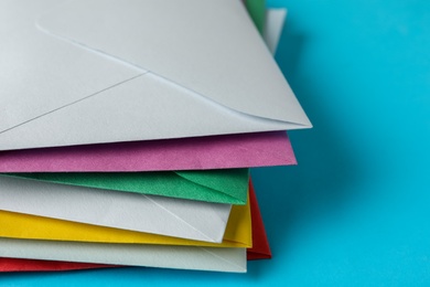 Photo of Stack of colorful paper envelopes on light blue background, closeup