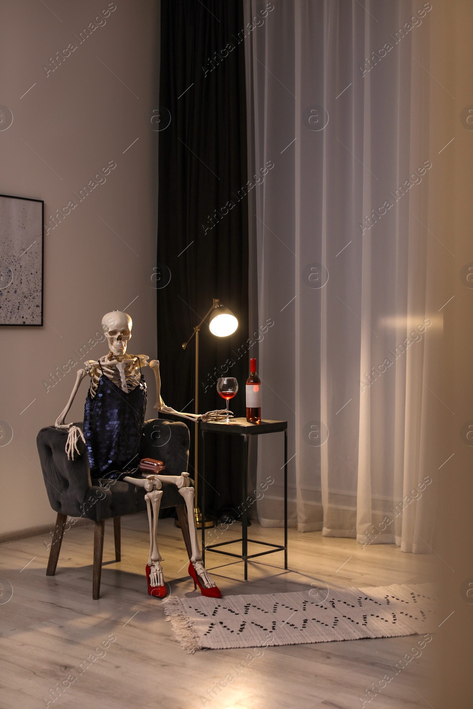 Photo of Skeleton in dress with wine sitting at table indoors