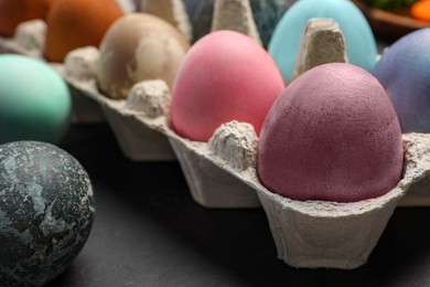 Photo of Easter eggs painted with natural organic dyes on black table, closeup. Space for text