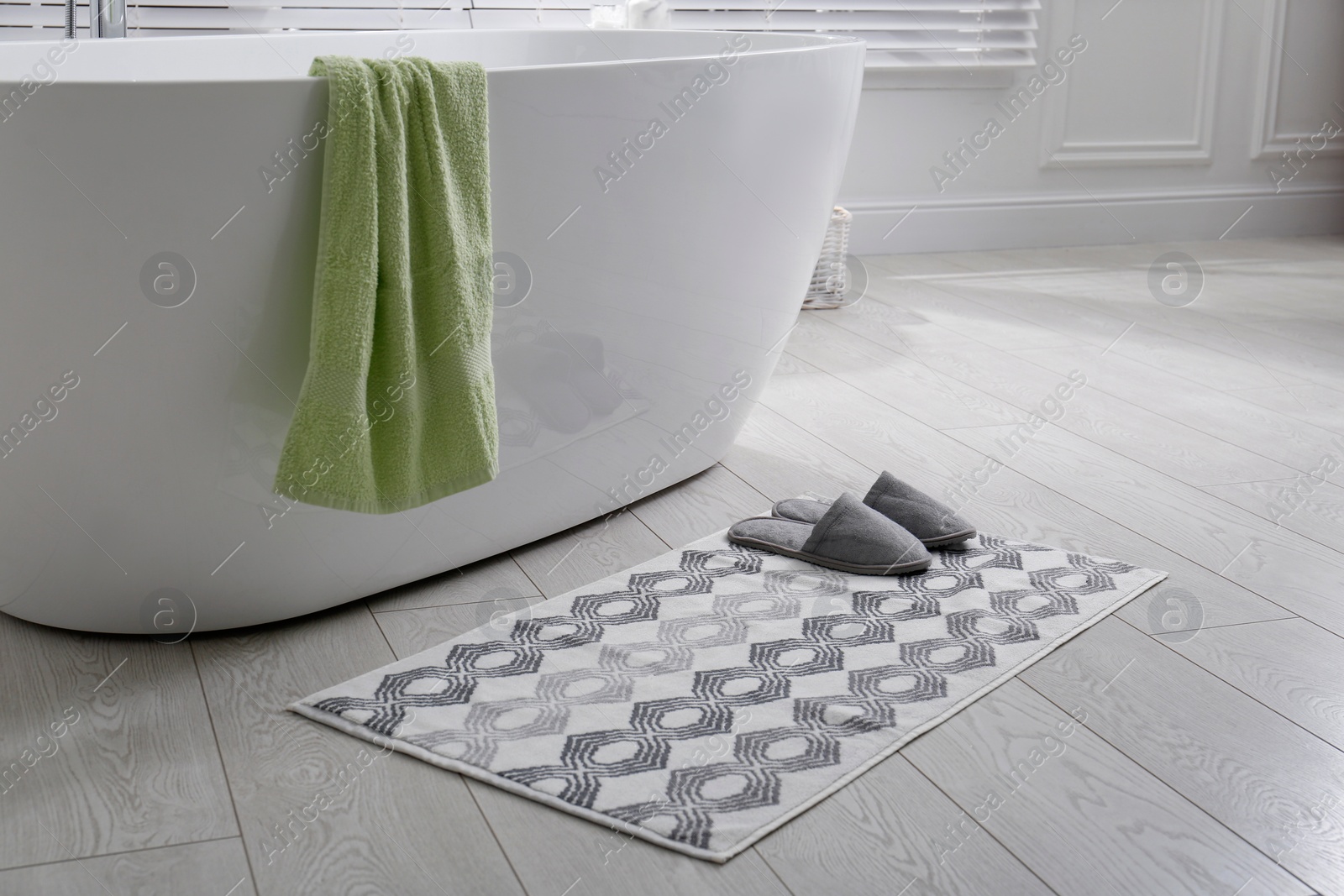 Photo of Stylish mat with slippers on floor near tub in bathroom. Interior design