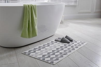 Photo of Stylish mat with slippers on floor near tub in bathroom. Interior design