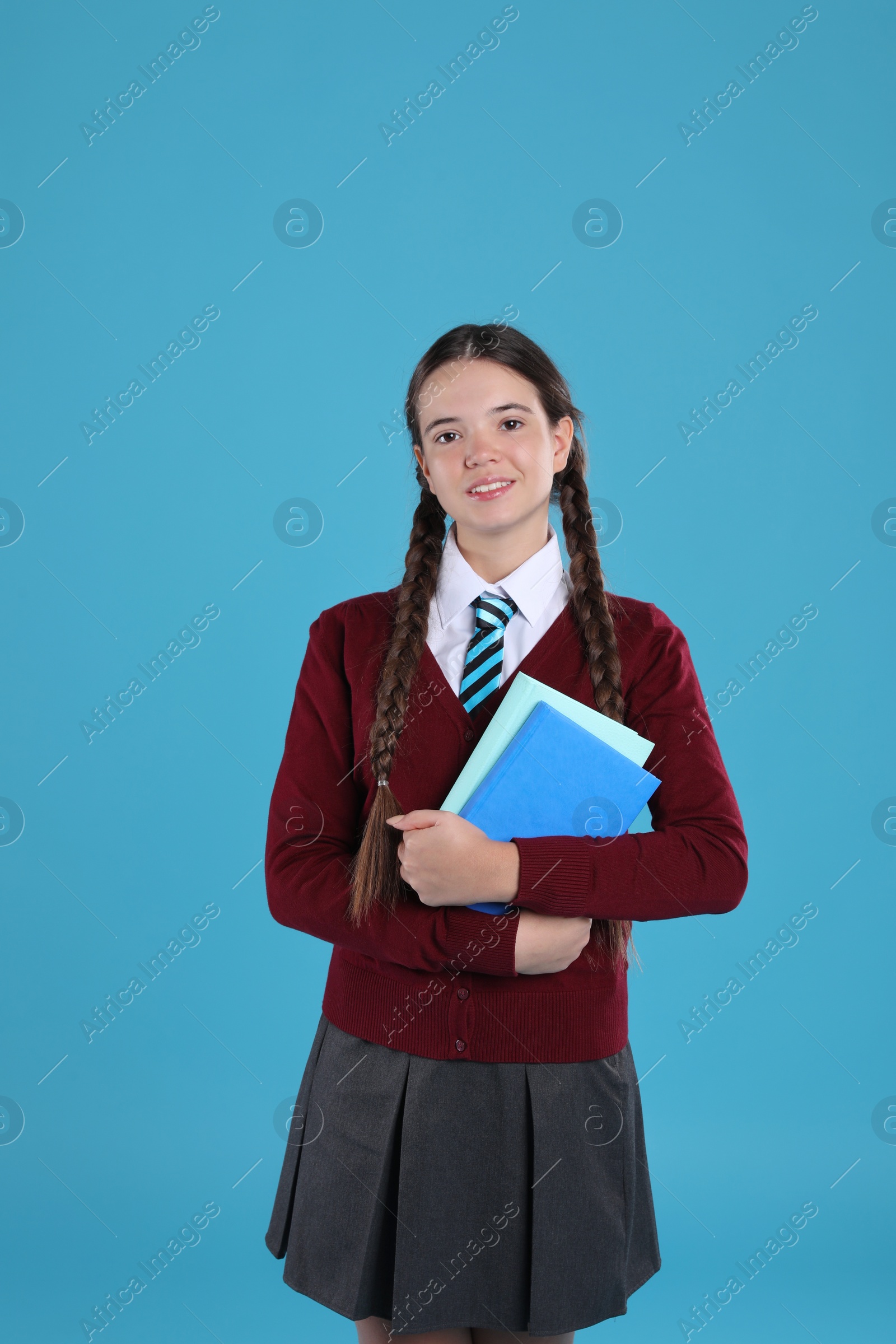 Photo of Teenage girl in school uniform with books on light blue background