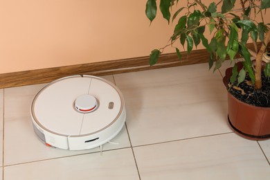 Robotic vacuum cleaner and fallen yellow leaves near houseplant indoors