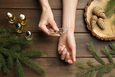 Photo of Woman applying pine essential oil on wrist at wooden table, top view