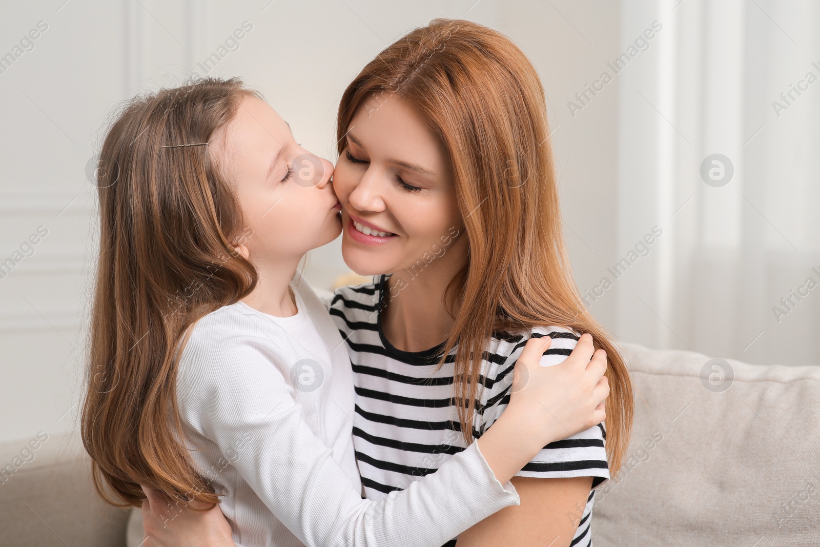 Photo of Cute daughter kissing her mom on sofa at home