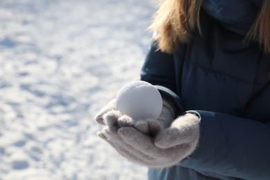 Woman holding snowball outdoors on winter day, closeup. Space for text