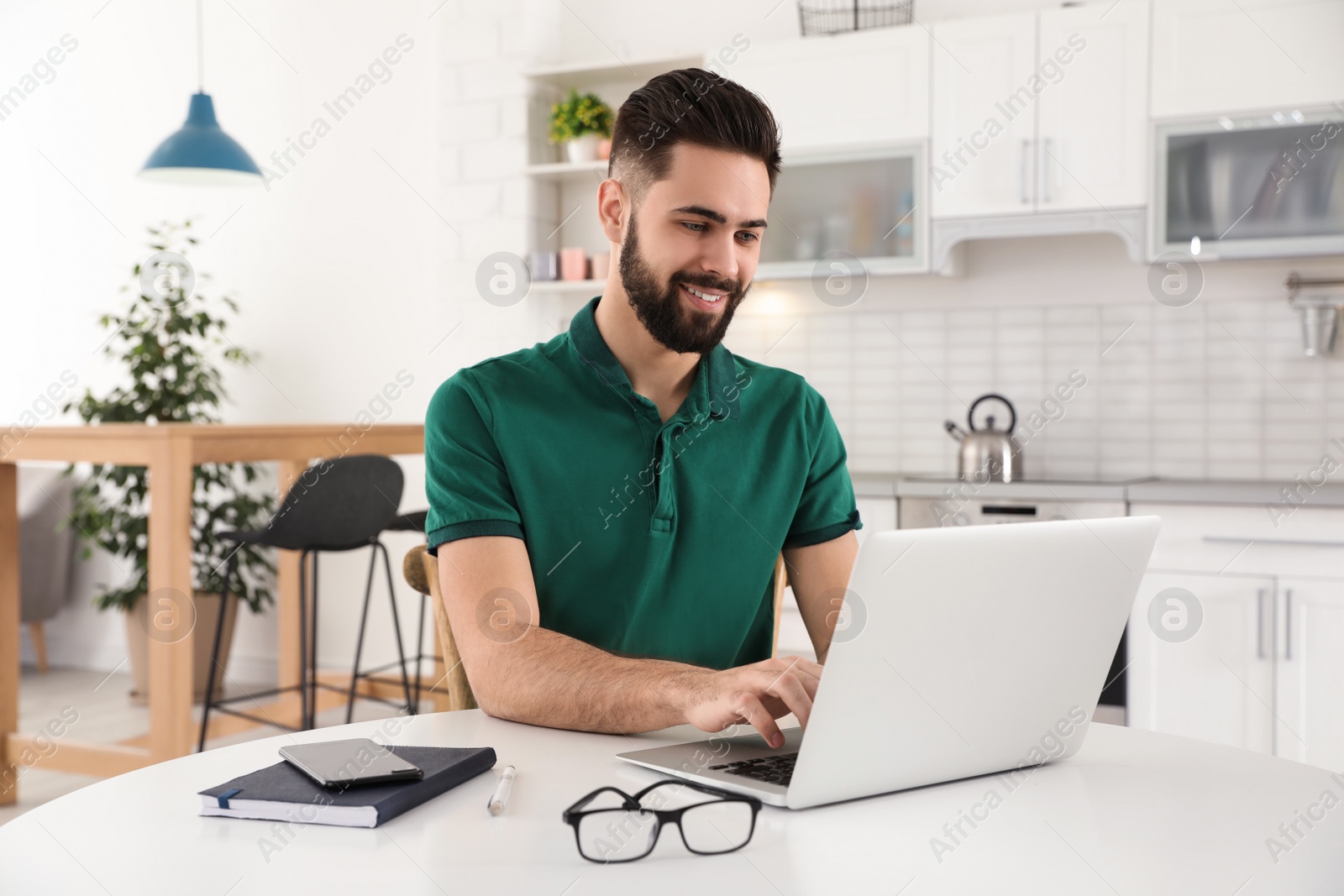 Photo of Handsome young man working with laptop at table in kitchen