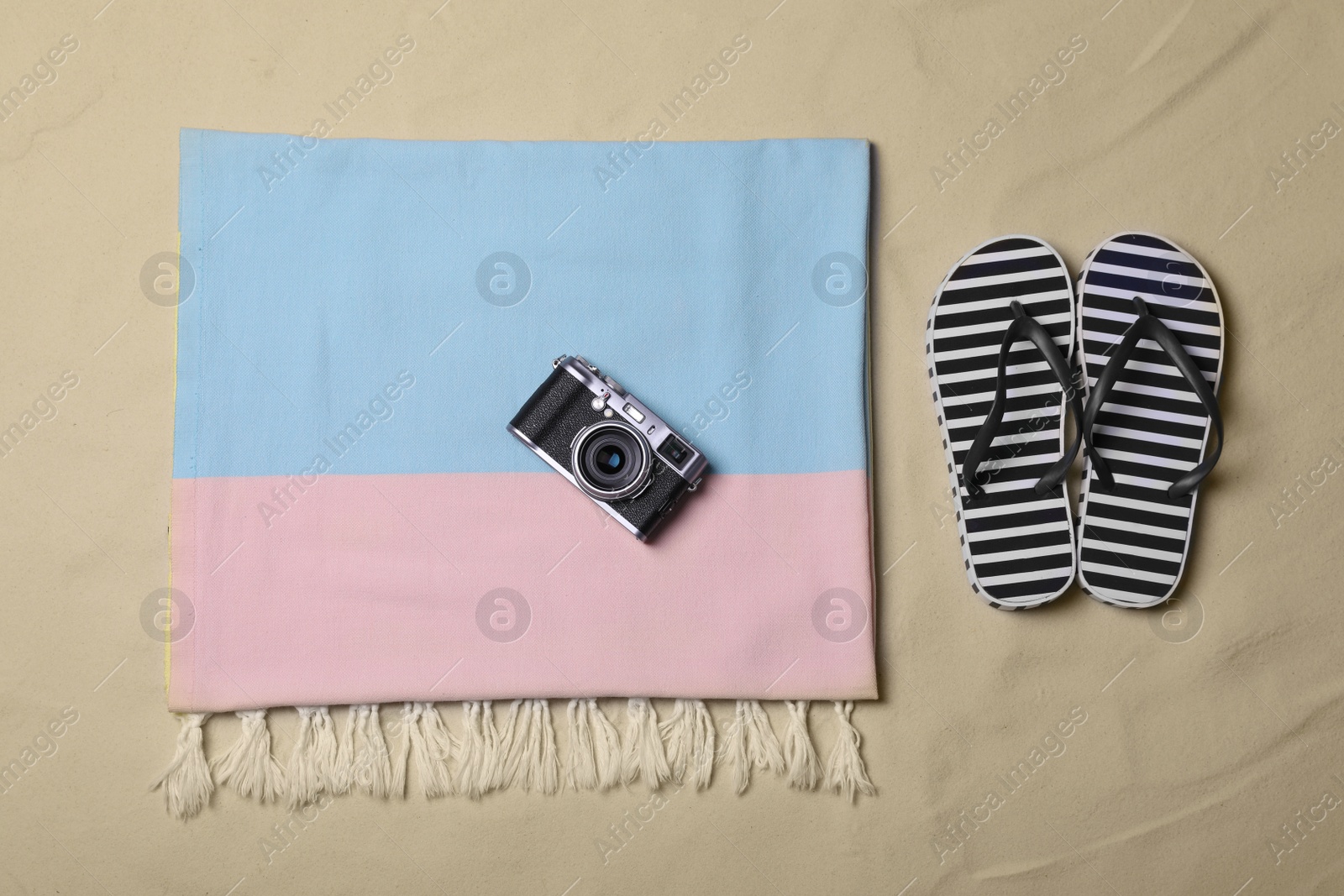 Photo of Beach towel, camera and flip flops on sand, flat lay