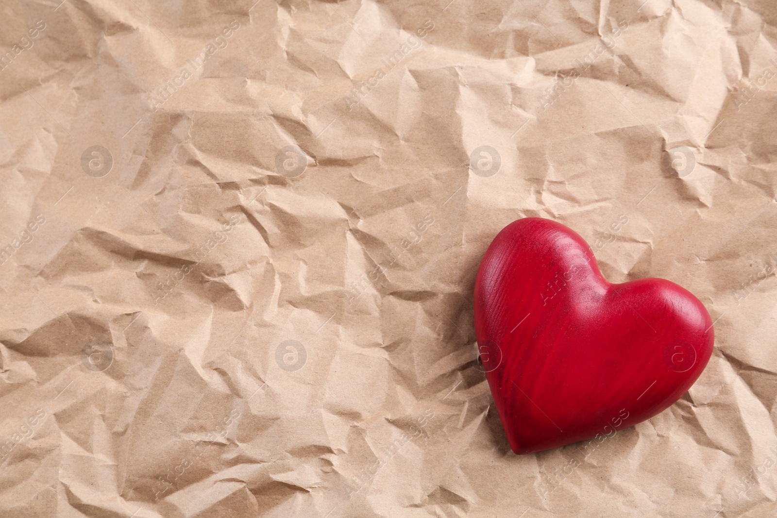 Photo of Red wooden heart on crumpled kraft paper, top view with space for text. St. Valentine's day