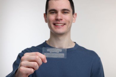 Young man with whitening strips on light background