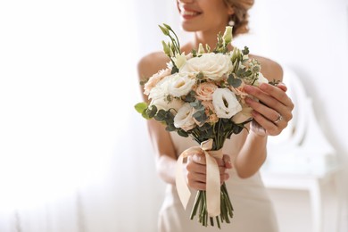 Young bride with beautiful wedding bouquet in room, focus on flowers. Space for text