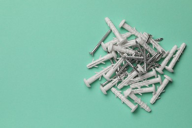 Photo of Many metal screws and white dowels on turquoise background, flat lay. Space for text