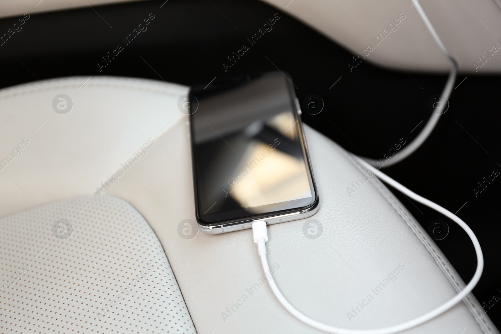 Photo of Mobile phone with charging cable in car, closeup