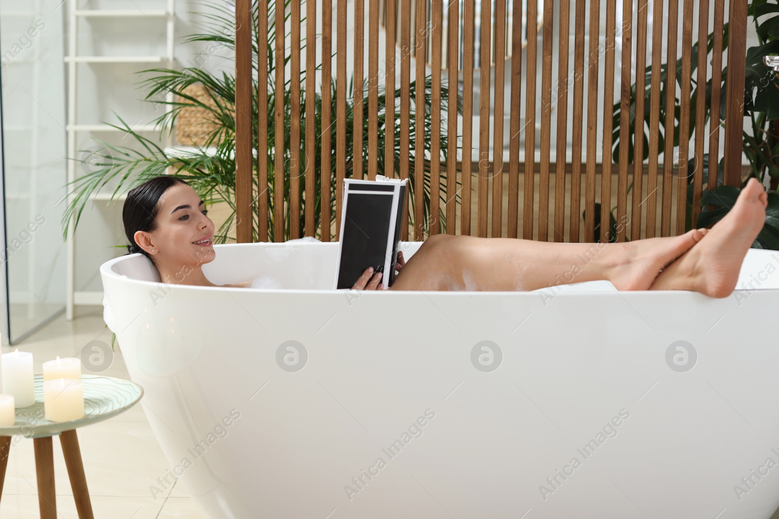 Photo of Beautiful young woman reading book while taking bath at home