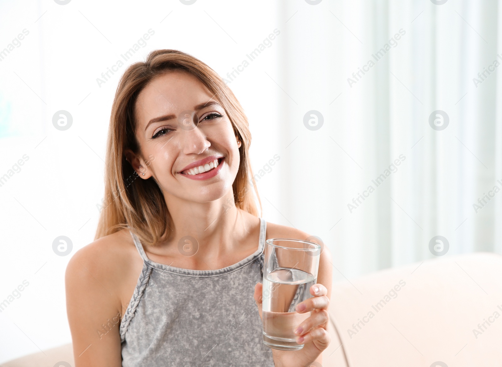 Photo of Young woman holding glass with clean water at home. Space for text