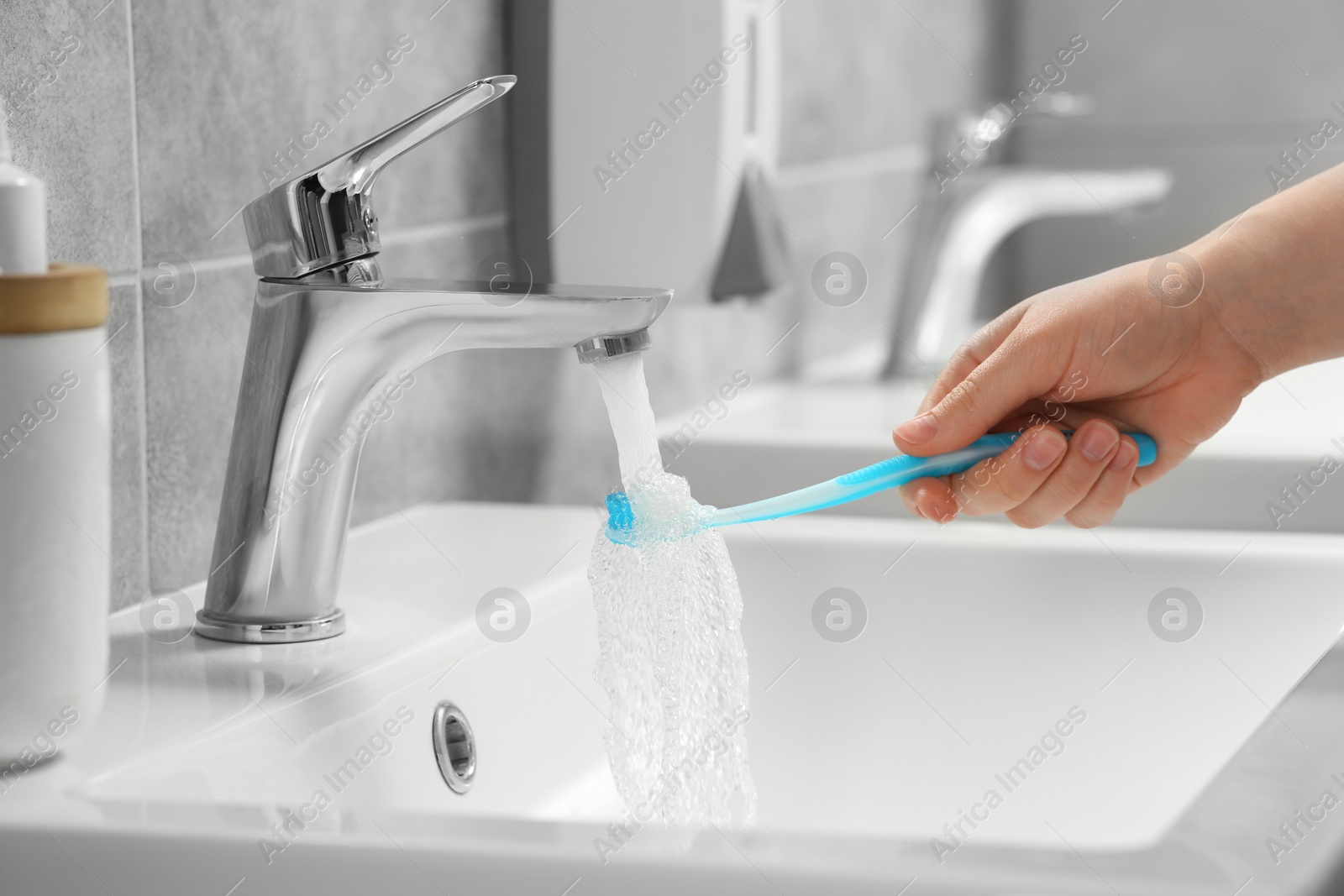 Photo of Woman washing plastic toothbrush under flowing water from faucet in bathroom, closeup