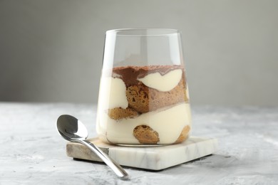 Photo of Delicious tiramisu in glass and spoon on grey textured table, closeup