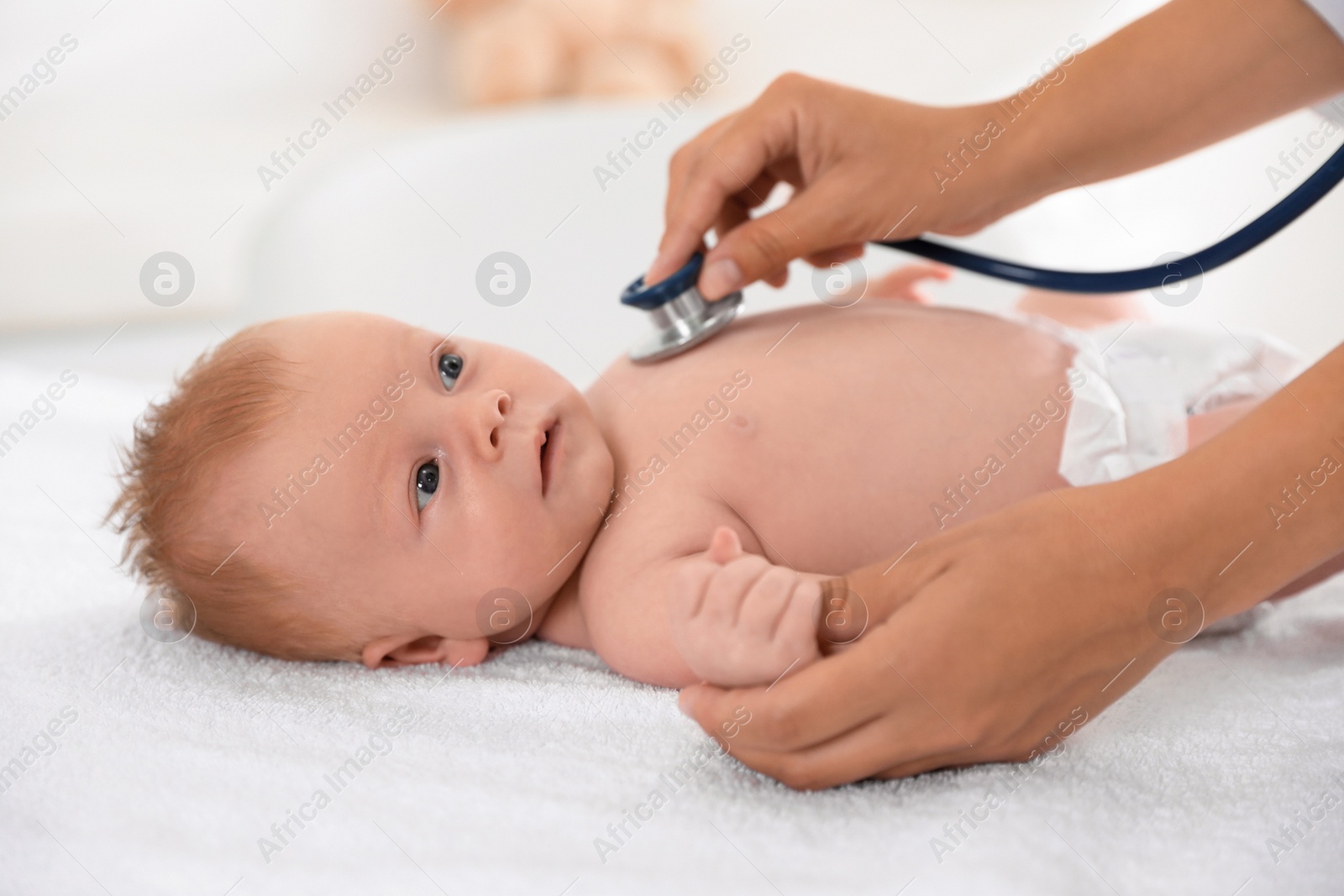 Photo of Doctor examining cute baby with stethoscope indoors, closeup. Health care