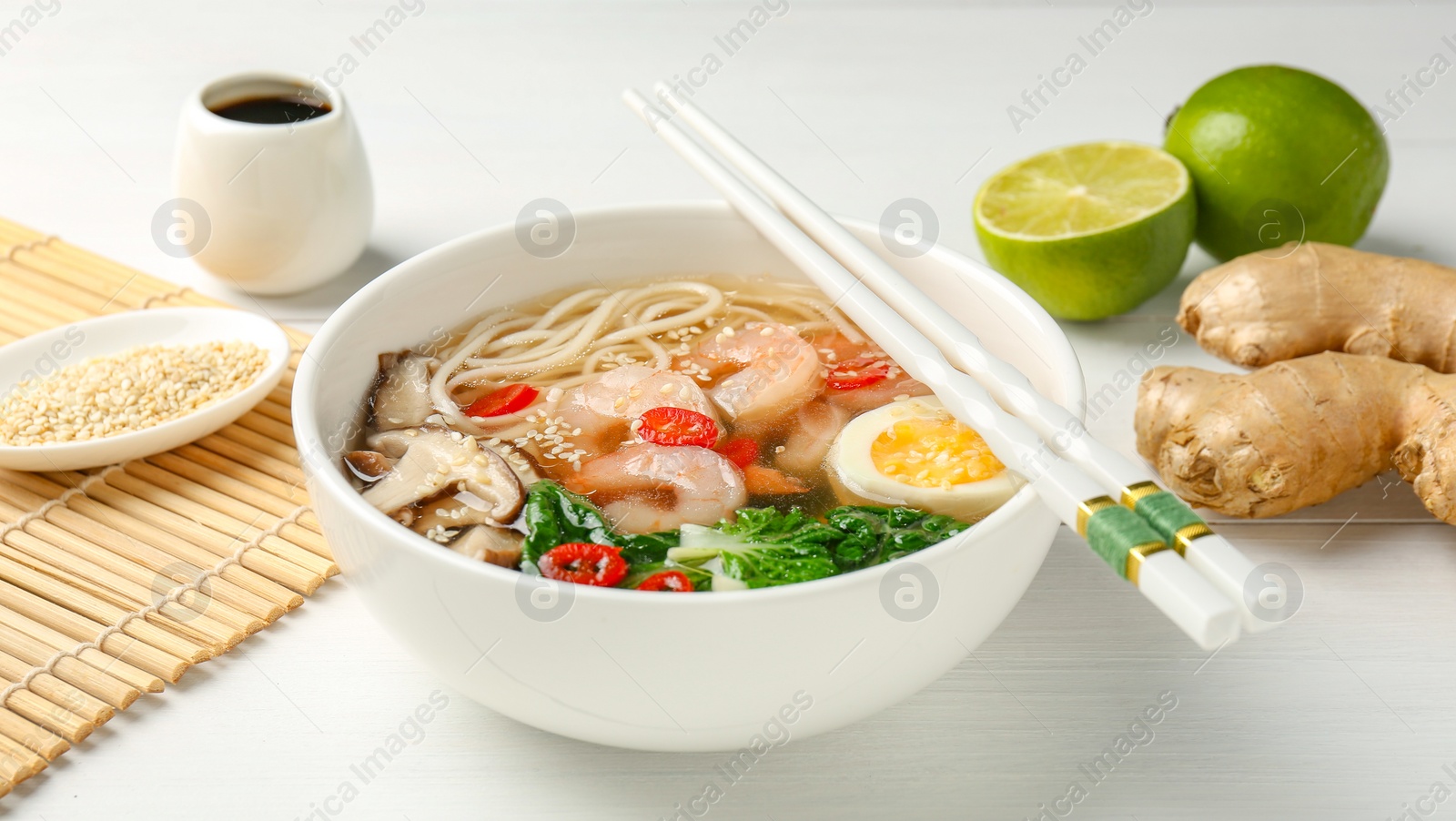 Photo of Tasty ramen with shrimps in bowl and chopsticks on white table