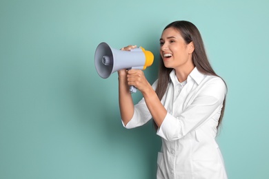 Photo of Young female doctor using megaphone on color background