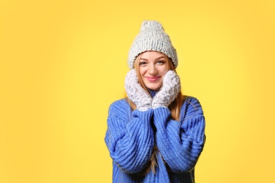 Portrait of emotional young woman in stylish hat, sweater and mittens on color background. Winter atmosphere