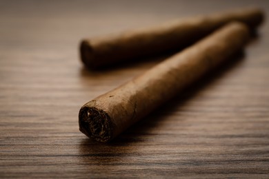 Photo of Cigars wrapped in tobacco leaves on wooden table, closeup