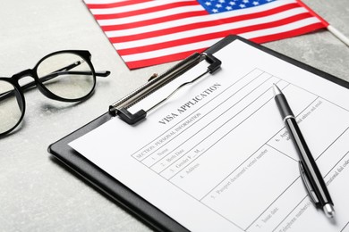 Photo of Visa application form, glasses and American flag on light grey table, closeup