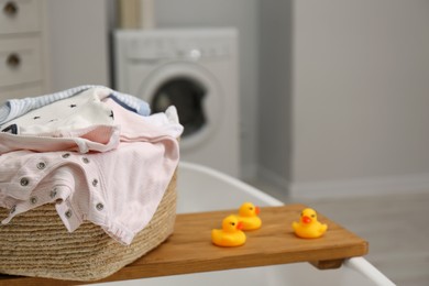 Laundry basket with baby clothes on tub tray in bathroom, closeup. Space for text